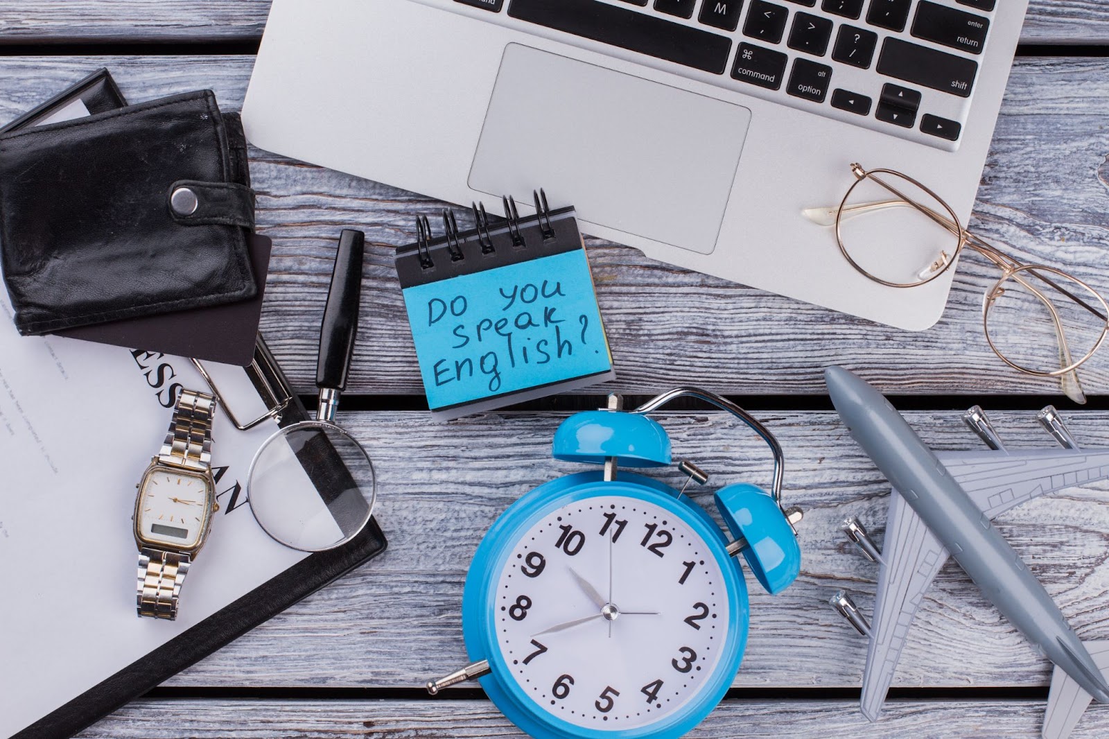 Workspace with laptop, alarm clock, and note saying 'Do you speak English?' — TOEFL preparation